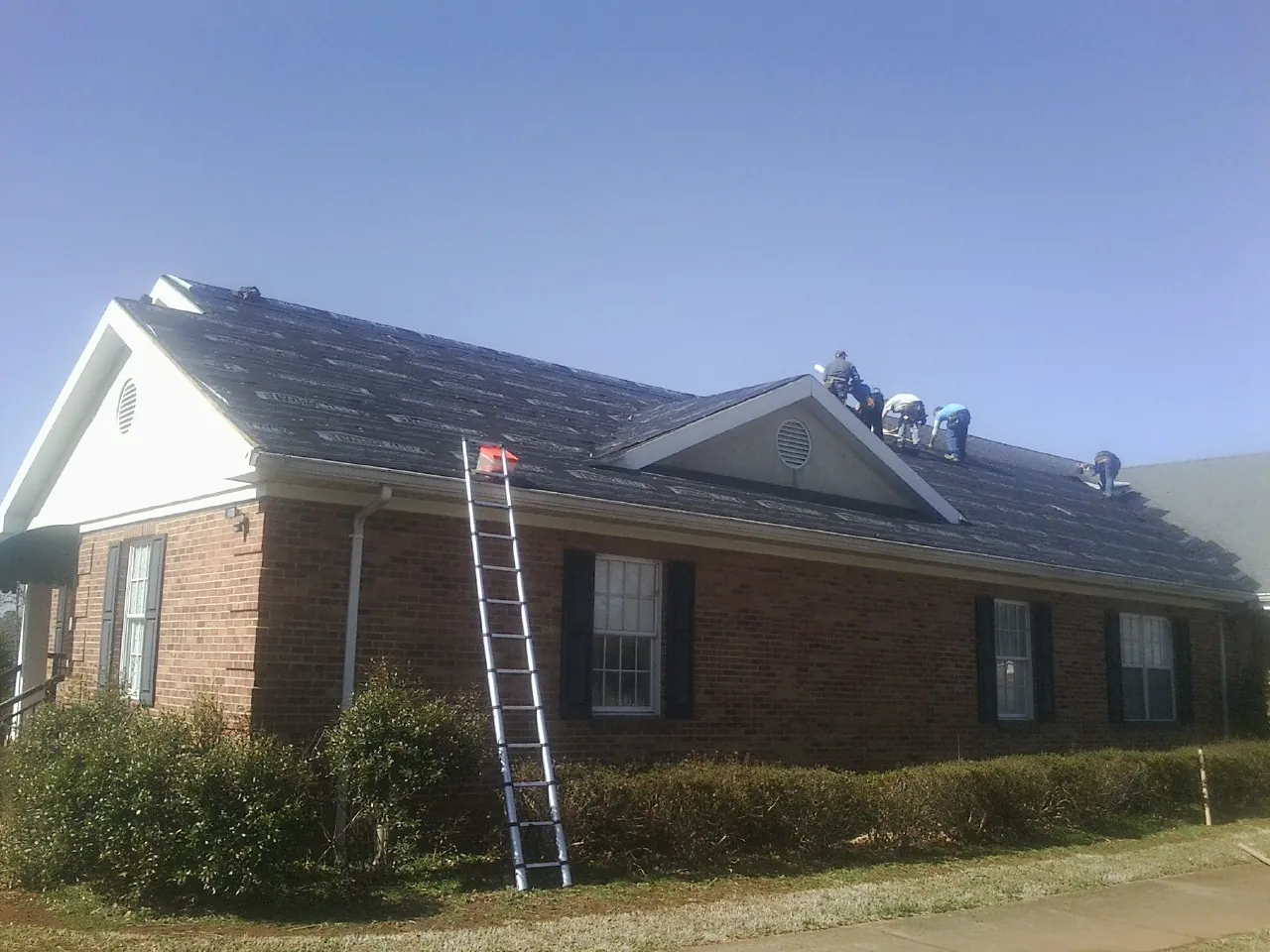 Crew tearing shingles off a brick ranch roof with a ladder set — Emergency Roof Repair work by our crew in Craig