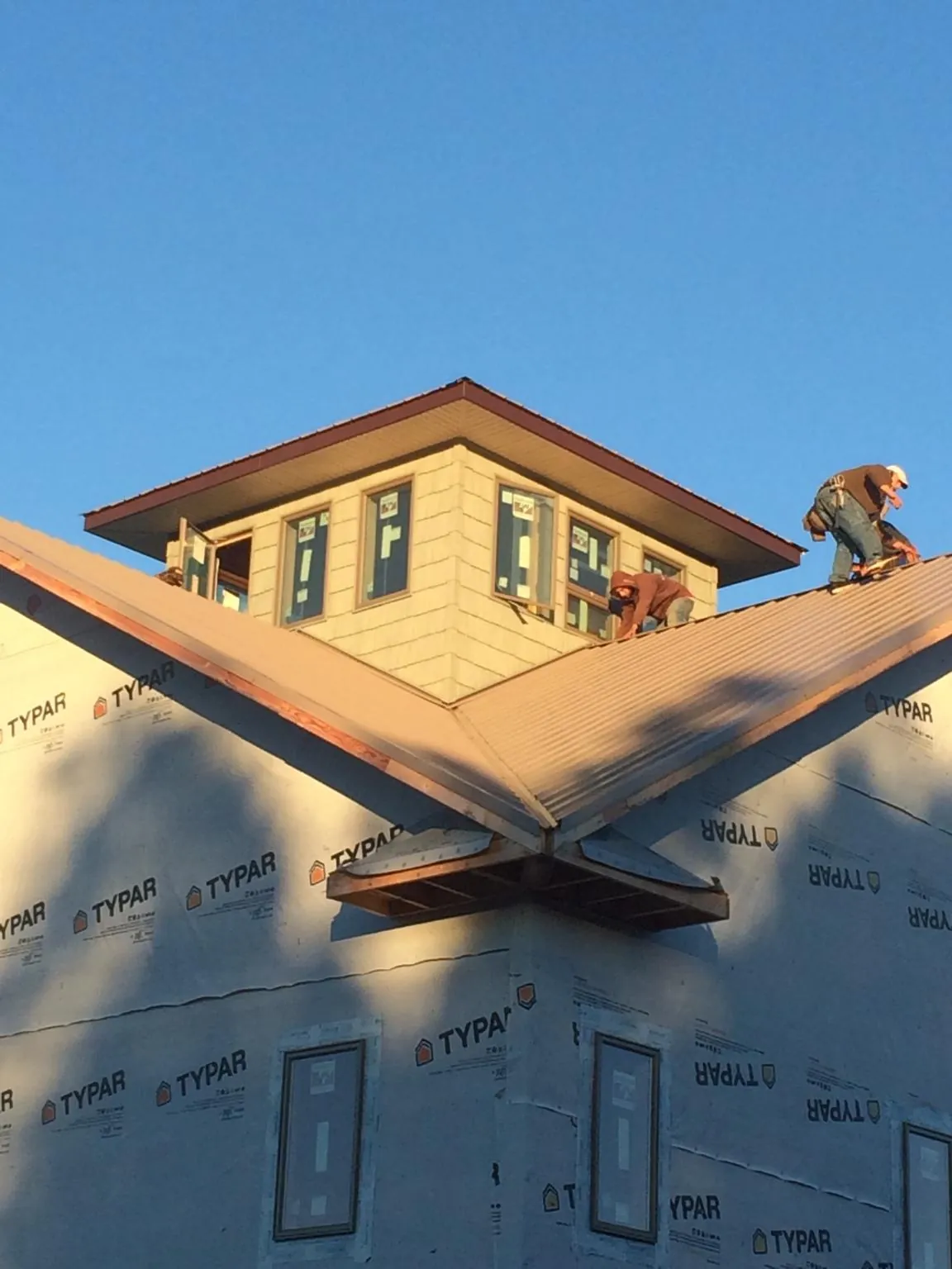 Roofers working around a rooftop cupola on a new metal roof at sunset — Roof Waterproofing in Craig by Roofing Brothers